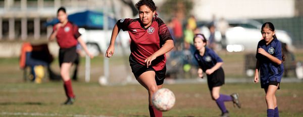 A Region 13 player in a red and black uniform chases the ball during a game